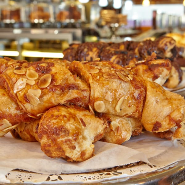 Golden-brown almond croissants with flaky crusts and sliced almonds on a white paper doily.