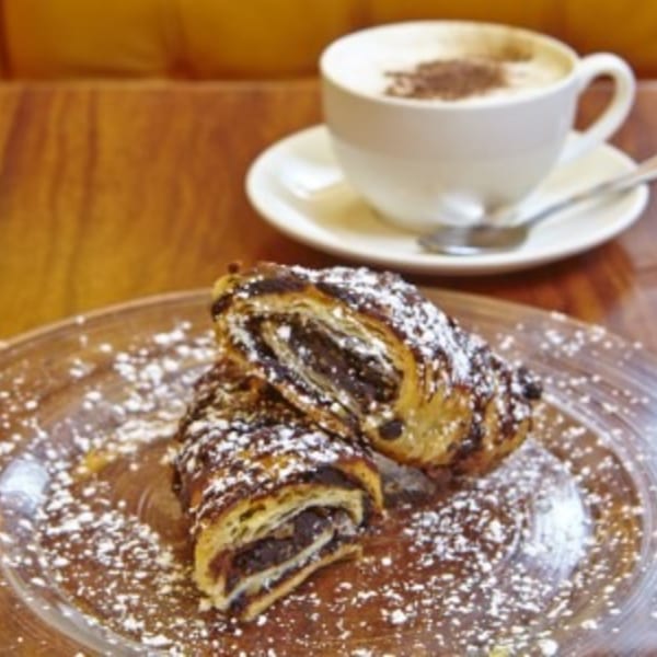 Chocolate croissants dusted with powdered sugar on a plate with a cup of coffee.
