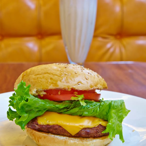 A Jax Inn Diner cheeseburger with lettuce and tomato, with a milkshake in the background.